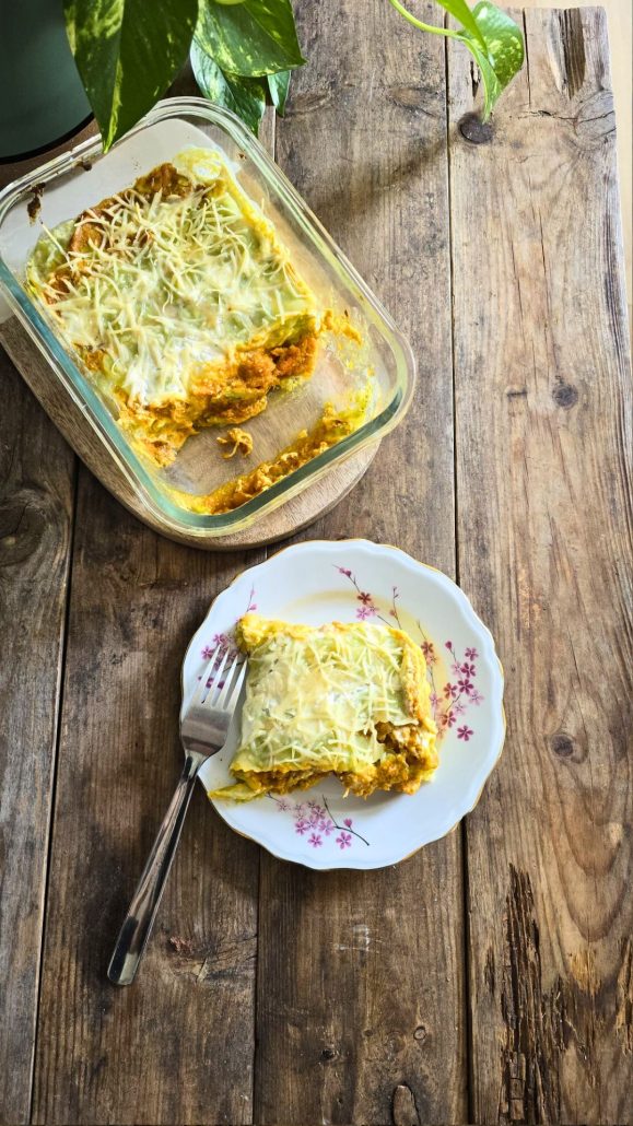 Une part de gratin de ravioles à la courge butternut coupée dans une assiette, posée à côté du plat à gratin